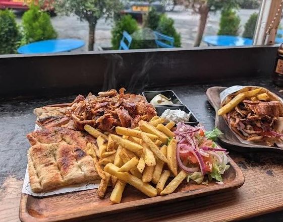 Open gyros platter with seasoned fries, salad and a wrapped gyros at the window table